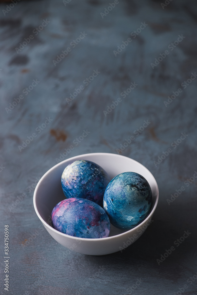 
Easter colored eggs in a white bowl on a textured blue background.