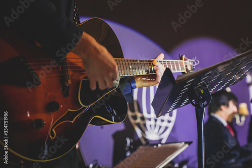 Concert view of an electric guitar player with vocalist and musical jazz band orchestra performing in the background, guitarist on the stage