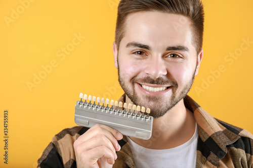 Young man with teeth color samples on yellow background