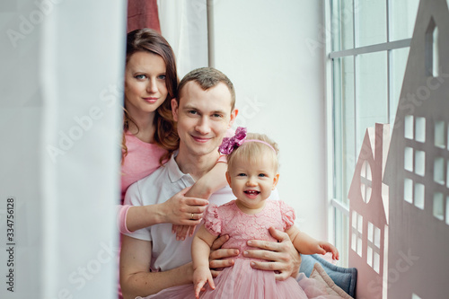 Happy family sitting on windowsill together. Family smiling while sitting in front of window