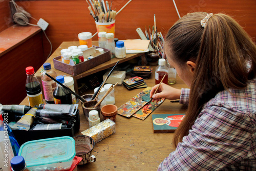 Girl artist paints a picture in the studio. Reproduction of the icon of St. Nicholas. Workflow of the artist in the studio. Brushes and paints on the background art workplace. photo