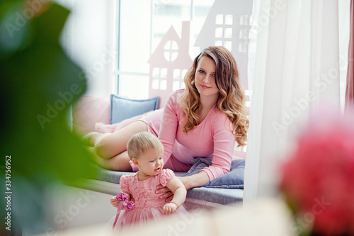 mother plays with her daughter at the window in pink dresses. mother's day.