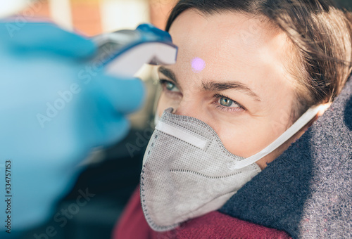 Temperature check point - the woman behind the wheel of the car in an anti-virus mask is subjected to temperature measurement.