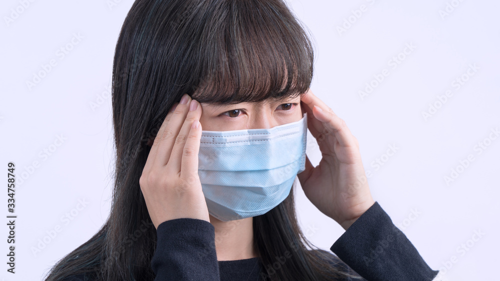 Young woman is feeling dizzy, headache, sick, unwell with wearing a medical blue face mask over the gray background, close up, copy space. Young woman is feeling dizzy, headache, sick, unwell with wearing a medical blue face mask over the gray background, close up, copy space.