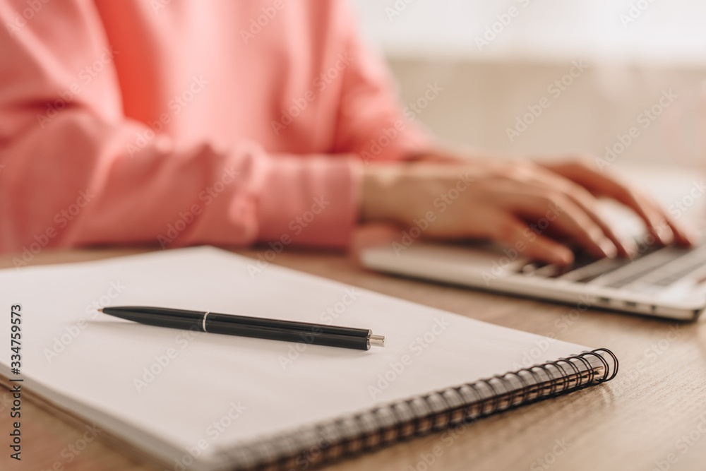 Cropped view of freelancer working with laptop near notebook with pen at table Cropped view of freelancer working with laptop near notebook with pen at table