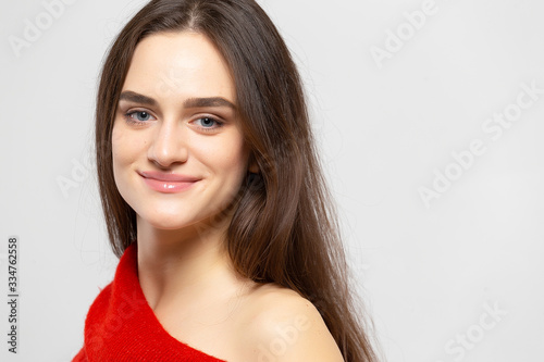 Portrait of a young beautiful woman with a light smile dressed in a red sweater on a light gray background.