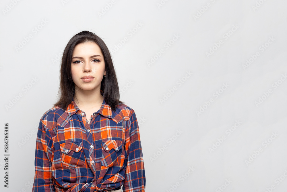 Portrait young beautiful woman not smiling in plaid shirt isolated on white-gray background. Girl with minimal natural make-up on her face. The photo is not retouched with natural defects on the skin. Portrait young beautiful woman not smiling in plaid shirt isolated on white-gray background. Girl with minimal natural make-up on her face. The photo is not retouched with natural defects on the skin.