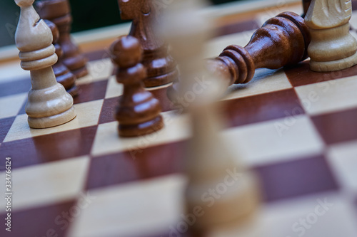 Intentionally crooked chessboard with blurred white king and toppled black king in the background, concept