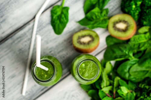  two green healthy smoothies made from apples, spinach, avocado, salad, kiwi on a wood background
