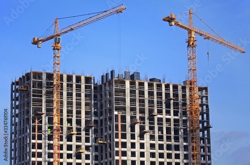 High-rise construction cranes and array of buildings under construction on the blue sky background. Building construction site with cranes. The construction of multifamily modern apartment buildings