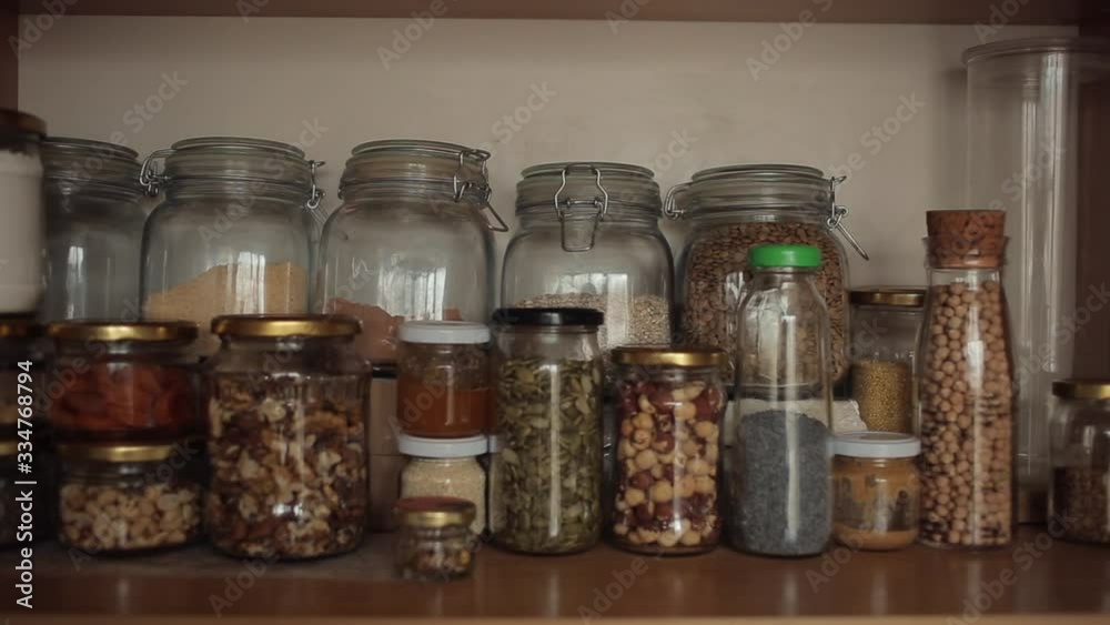The girl takes glass jars of groats from a shelf in the kitchen cupboard for cooking. Close-up The girl takes glass jars of groats from a shelf in the kitchen cupboard for cooking. Close-up