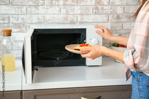 Woman putting plate with food in microwave oven