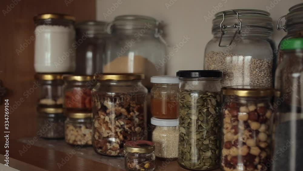 The girl arranges cans with groats and spices for cooking on a shelf in the kitchen cupboard. Close-up The girl arranges cans with groats and spices for cooking on a shelf in the kitchen cupboard. Close-up