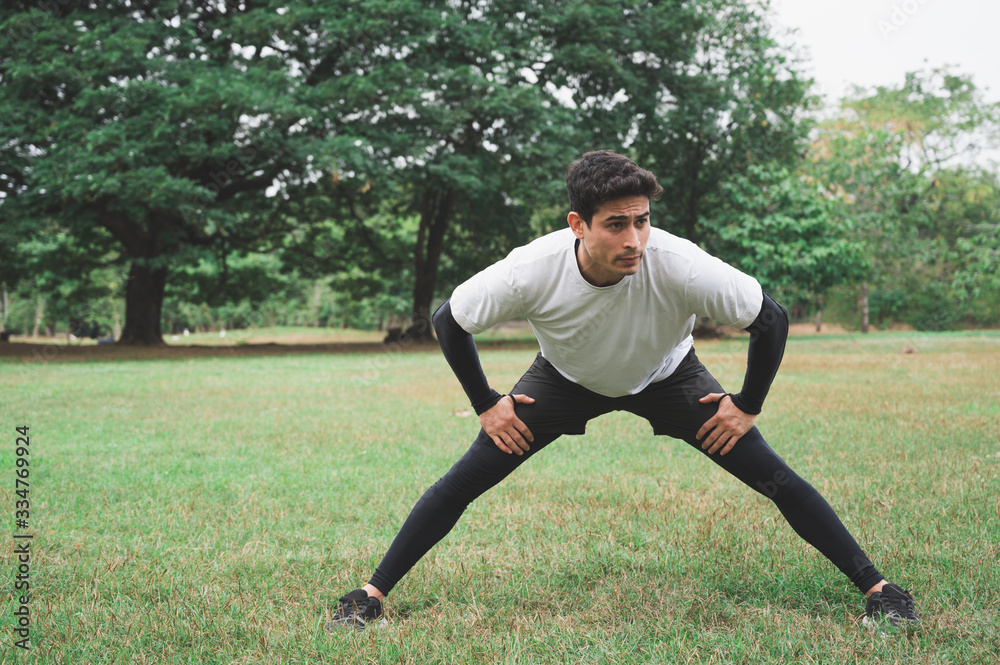 Young man runner stretching for warming up before running or working out in park. Young man runner stretching for warming up before running or working out in park.