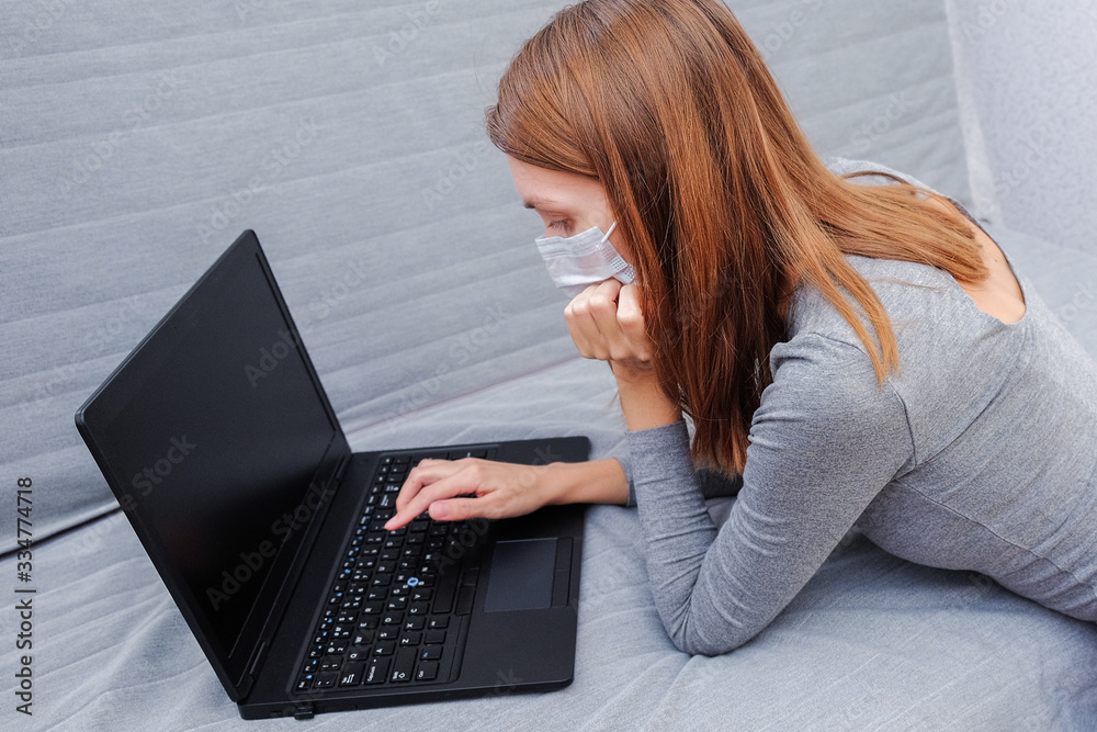 A young woman in a medical mask works at home on a laptop. Portrait of a woman surfing the Internet for online shopping, studying. A young woman in a medical mask works at home on a laptop. Portrait of a woman surfing the Internet for online shopping, studying.
