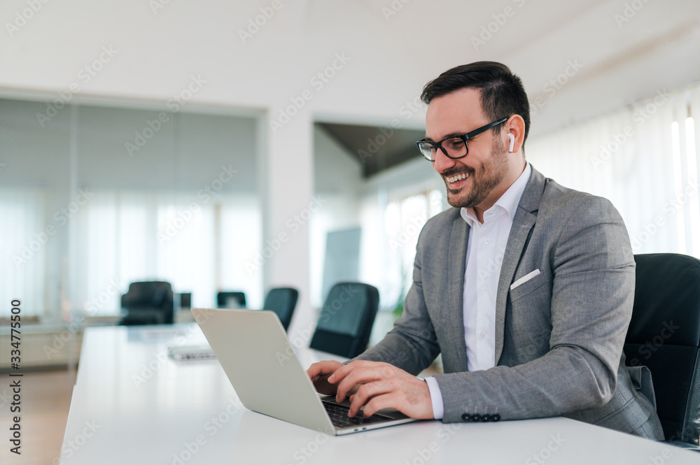 Portrait of a cheerful businessman using laptop at workplace. Listening to a music over wireless earphones. Portrait of a cheerful businessman using laptop at workplace. Listening to a music over wireless earphones.