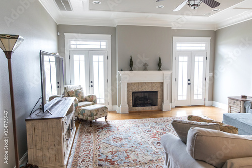 a bright and airy neutral beige living room den in a new construction house with a white and tiled fireplace as the main focal point as well as a decorative rug and lots of natural window light.