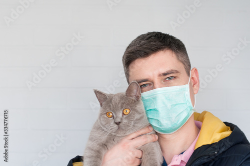 Portrait of european dark hair man in surgery face mask holding british cat on white background © Anastasia Rudenko