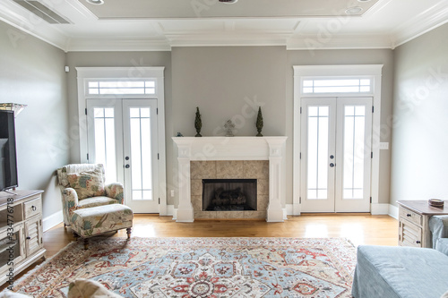 a bright and airy neutral beige living room den in a new construction house with a white and tiled fireplace as the main focal point as well as a decorative rug and lots of natural window light. photo