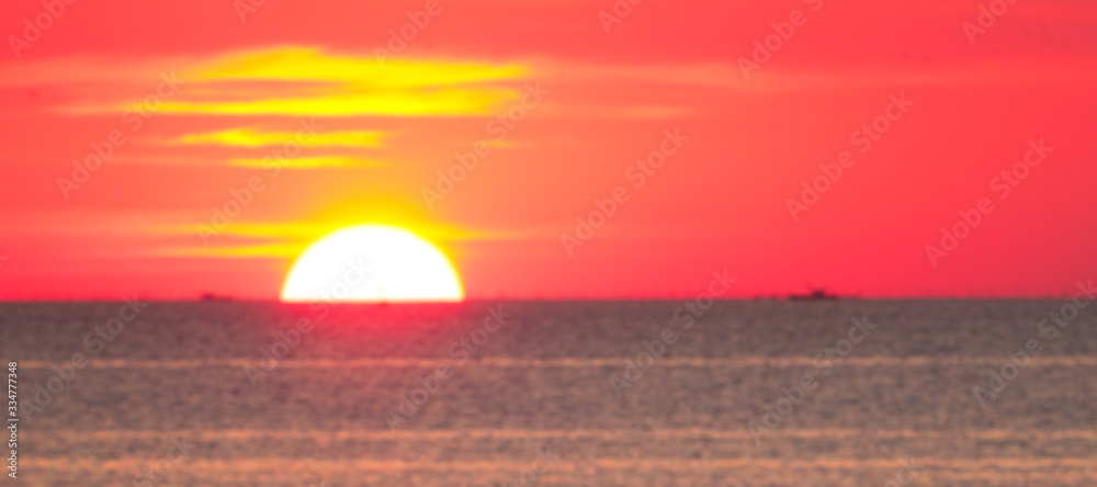 Blurry look of a big gorgeous sunset with silhouette of transportation boat passing by