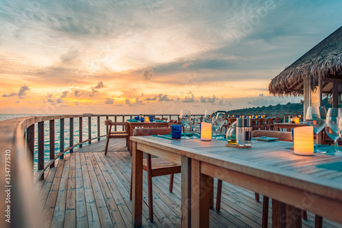 Fototapeta Naklejka Na Ścianę i Meble -  Romantic sunset on the shore of a tropical island. Outdoor restaurant with wooden deck and tables and chairs. Luxury hotel resort dinning view