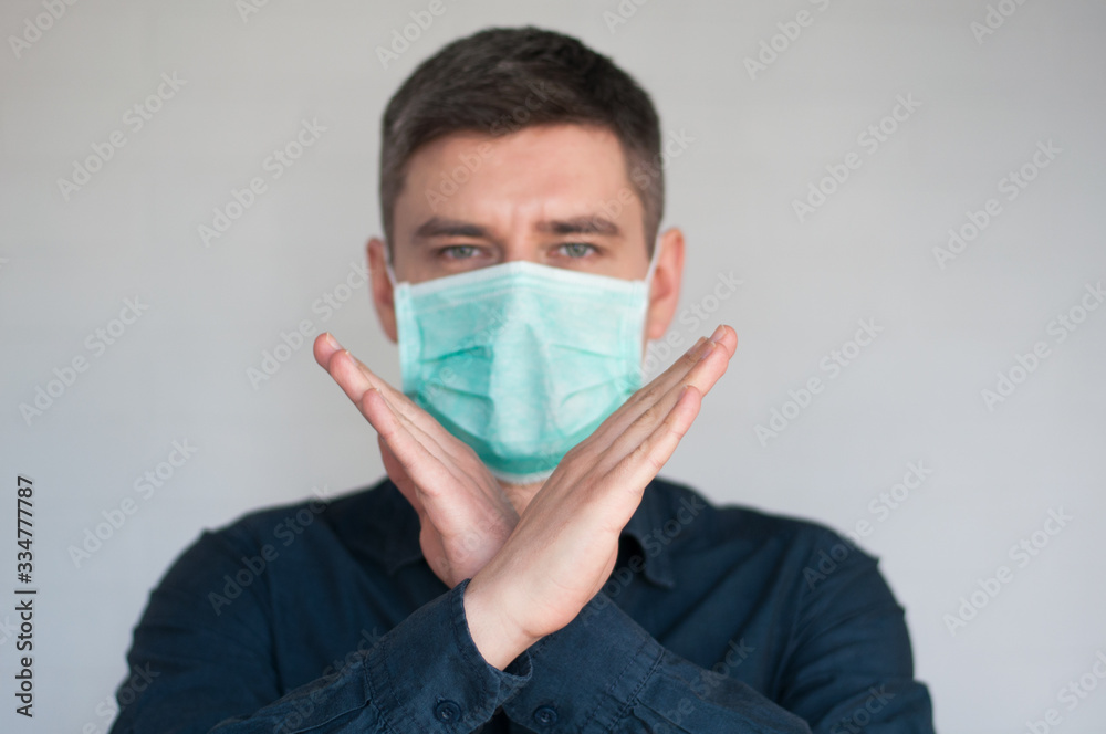 Portrait of european dark hair man in surgery face mask in blue shirt on gray background with crossed palms Portrait of european dark hair man in surgery face mask in blue shirt on gray background with crossed palms
