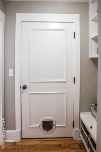 A white door to the garage with a pet cat dog small door and hardwood floors in a new construction home house