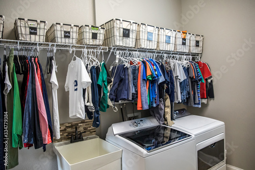 An organized laundry room with many clean shirts being hung to dry above a washer and dryer © Ursula Page