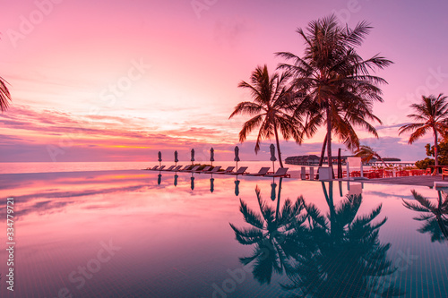 Beautiful poolside and sunset sky with palm trees silhouette. Luxurious tropical beach landscape  deck chairs and loungers and water reflection. Tranquil summer vacation  travel concept infinity pool