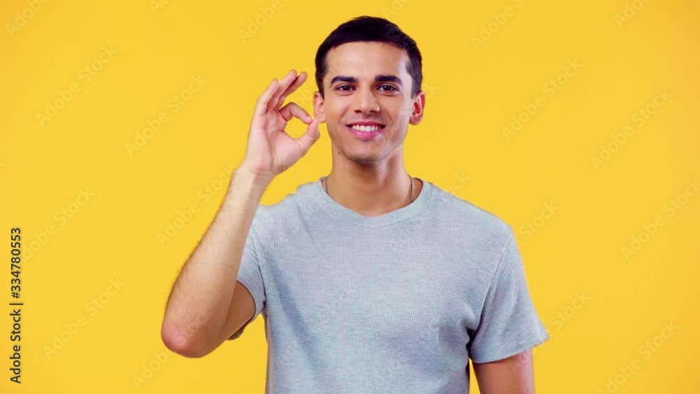 happy man showing okay gesture and smiling at camera isolated on yellow happy man showing okay gesture and smiling at camera isolated on yellow