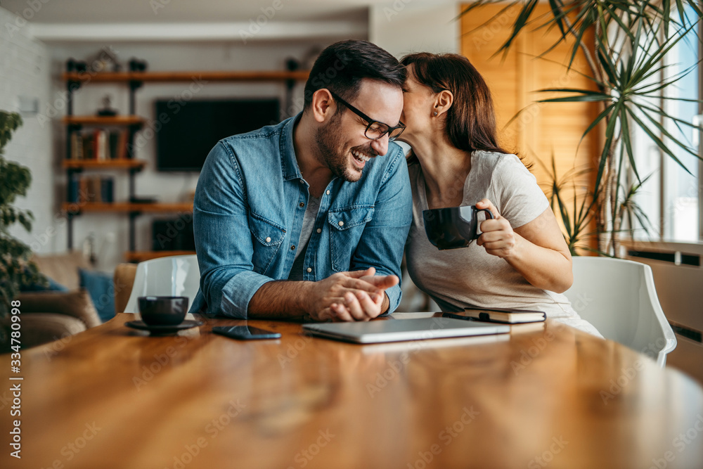 Portrait of a couple having fun at home. Woman whispering to man's ear, he is laughing. Portrait of a couple having fun at home. Woman whispering to man's ear, he is laughing.