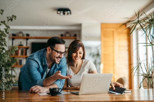 Portrait of a smiling couple looking at laptop together at cozy home office.