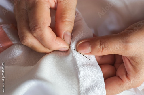Hand of the seamstress is using a needle and white thread to sew the seam on the shirt close-up.