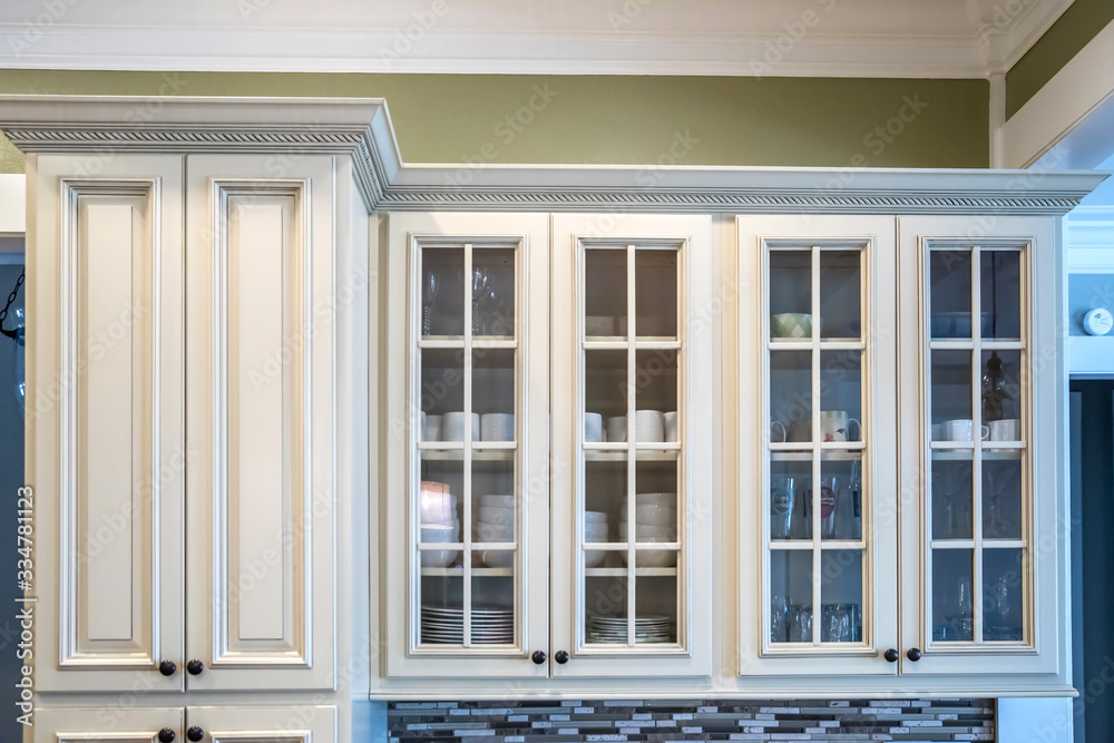 Glass door cabinets in a a square shaped green kitchen with cream colored cabinets in a new construction home with granite countertops and lots of cabinets and storage space Glass door cabinets in a a square shaped green kitchen with cream colored cabinets in a new construction home with granite countertops and lots of cabinets and storage space