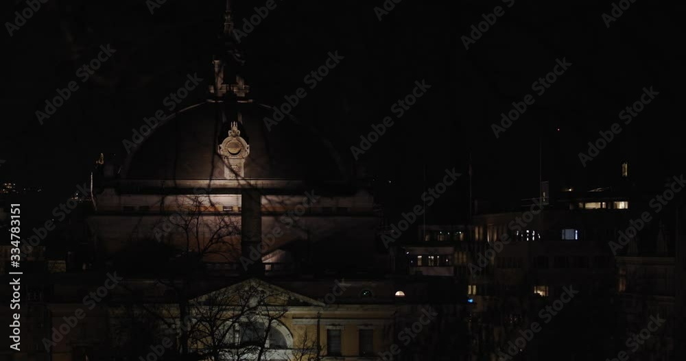 Wide night shot of the illuminated Norwegian National Theatre with its characteristic dome with decor on top, with trees in front of camera in parallax movement, in Karl Johan street in Oslo Norway.