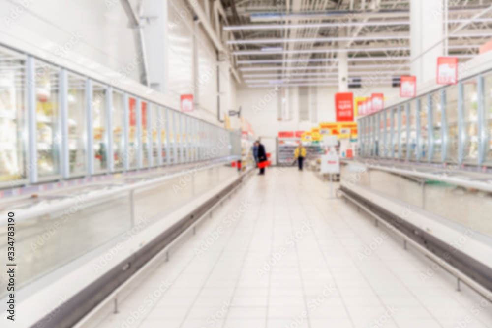 Naklejka premium Rows of frozen food display cases in a large supermarket. Blurred.