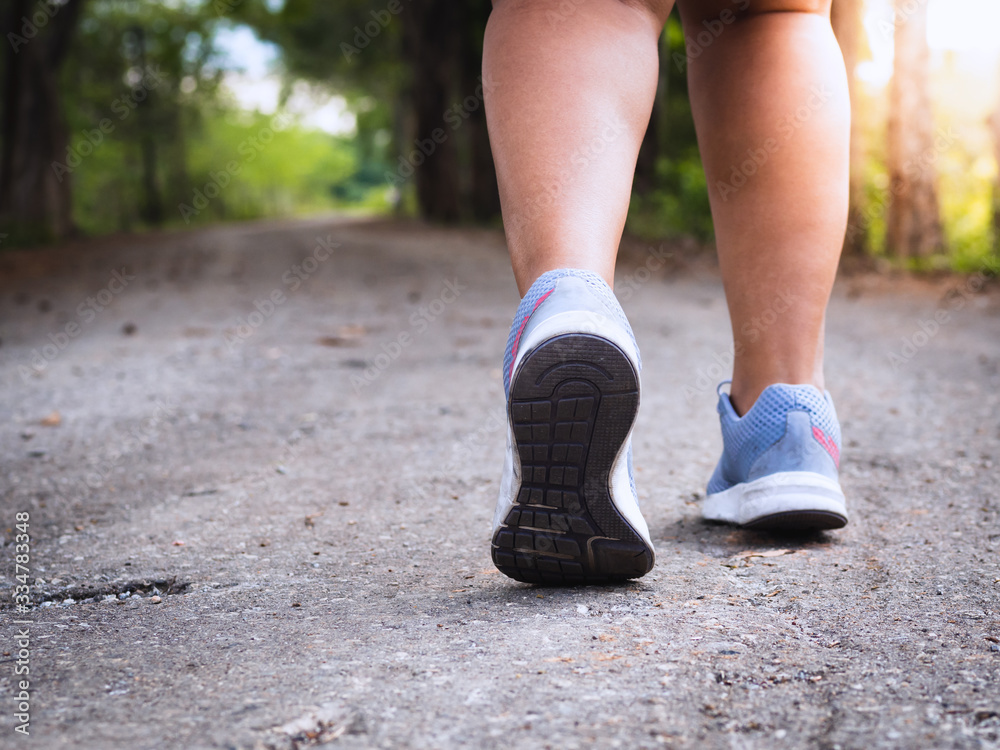 The fat woman's legs wear running shoes, walking or running in the garden