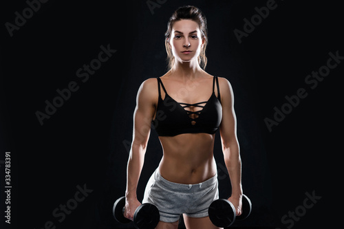 athletic young woman doing a fitness workout with dumbbells on black studio background