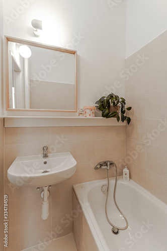 Empty small bathroom with white walls  tiles  sink and bath