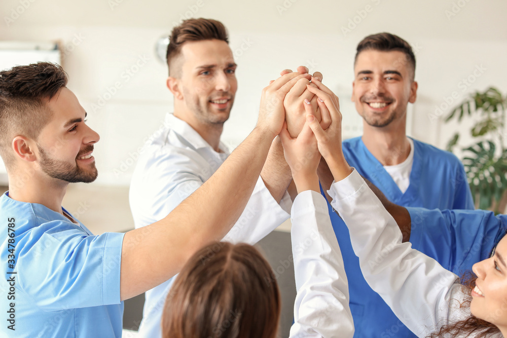 Fototapeta premium Group of doctors putting hands together in clinic. Unity concept