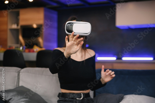 VR. Excited Millennial Girl Using Virtual Reality Headset Playing Videogame Indoor. Selective Focus