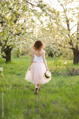 Young attractive woman with curly hair walking in a green flowered garden. Spring romantic mood photo