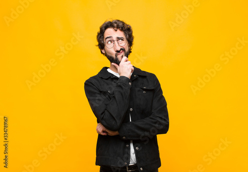 young crazy handsome man thinking, feeling doubtful and confused, with different options, wondering which decision to make against orange wall photo