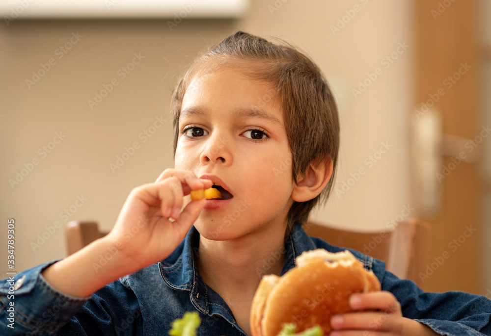 Little boy indoors eating a burger Little boy indoors eating a burger