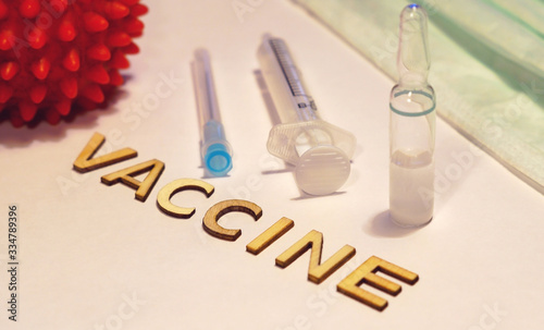 The word vaccine is laid out on a hundred table surrounded by an ampoule and syringe  