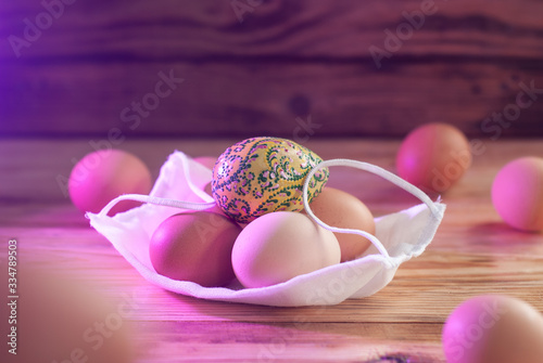 Easter eggs and a medical mask on a wooden table. Easter during the pandemic. purple contour light