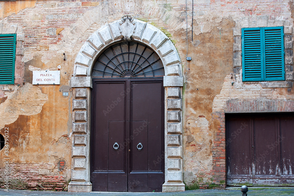 old massive iron doors in a medieval house with dilapidated plaster on the wall, Piazza del Conte, Siena, Italy old massive iron doors in a medieval house with dilapidated plaster on the wall, Piazza del Conte, Siena, Italy