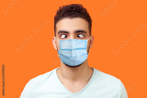 Portrait of comic crazy positive brunette man with surgical medical mask looking cross-eyed, having fun with silly face expression, playing fool. indoor studio shot isolated on orange background photo