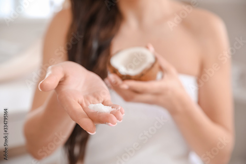 Beautiful young woman applying coconut oil on her hair at home, closeup