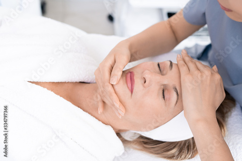Close-up of aesthetic professional sculpting face of mature woman with massage, relaxed woman enjoying beauty treatment procedure